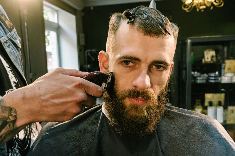 Barbeiro aparando a barba de um cliente