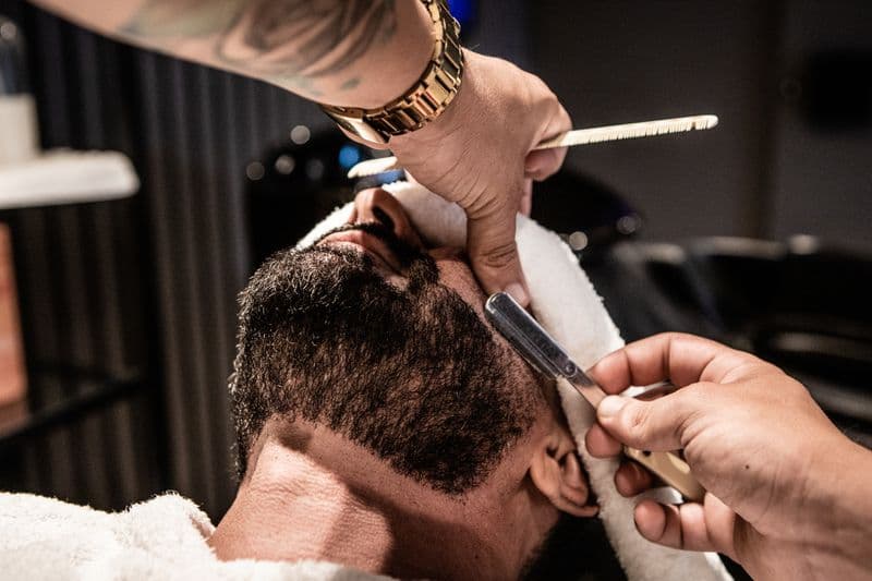 Barbeiro fazendo acabamento fino com navalha no rosto do cliente